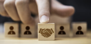Hand putting hand shaking which print screen on wooden cube block in front of human icon for business deal and agreement concept.